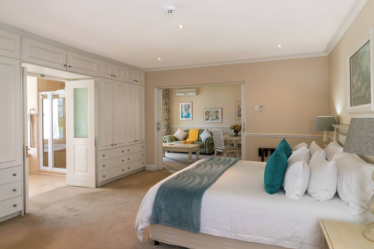 A bedroom with a large bed, a desk, and a chair. There is a door leading to another room.