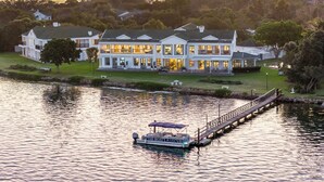 A large, multi-story hotel with a waterfront view, a dock with a boat, and a well-maintained lawn. - St James of Knysna (Knysna)
