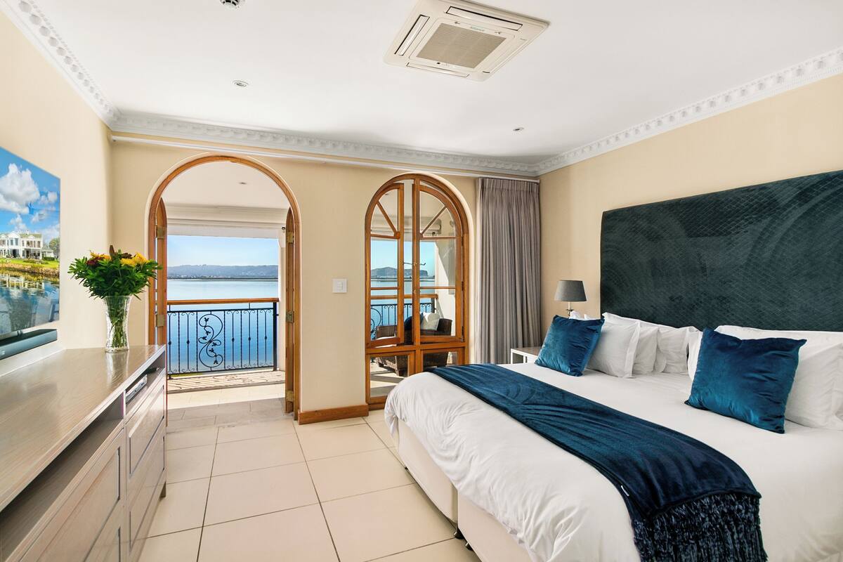 A hotel room with a large bed, a desk, and a view of the sea through an open archway.
