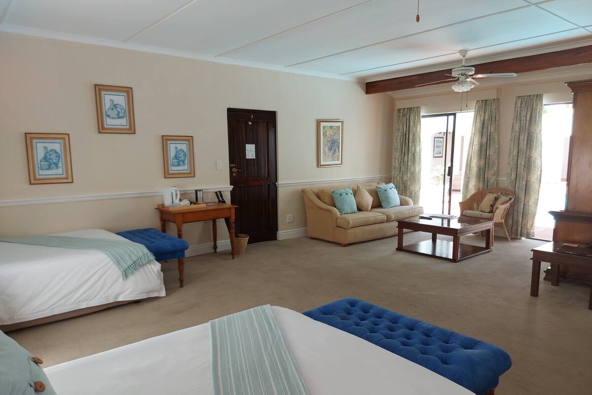 A hotel room with two beds, a sofa, a chair, a small table, and a ceiling fan.