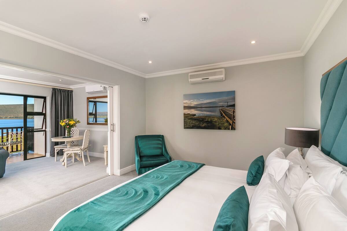 A hotel room with a bed, a desk, and a chair. There is a balcony with a view of the sea.