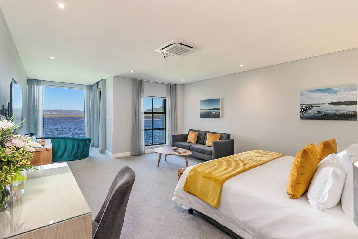 A hotel room with a bed, a sofa, a desk, and a view of the sea.