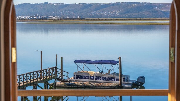 A balcony with a view of a calm lake, a dock with a boat, and a table with a bottle and glasses. - St James of Knysna (Knysna)