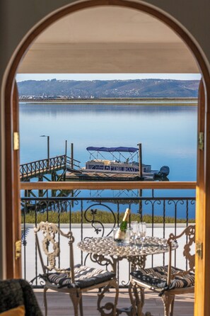 A balcony with a view of a calm lake, a dock with a boat, and a table with a bottle and glasses. - St James of Knysna (Knysna)