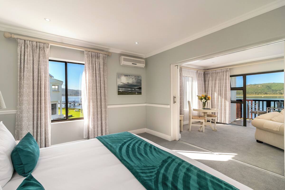 A hotel room with a large bed, a view of the outdoors, a balcony, and a dining area.