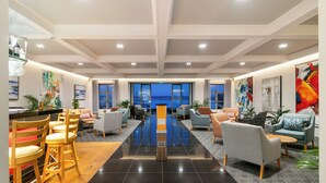 A modern hotel lobby with a central reflective black floor, seating areas with sofas and chairs, artwork on the walls, and a view of the cityscape through large windows. - St James of Knysna (Knysna)
