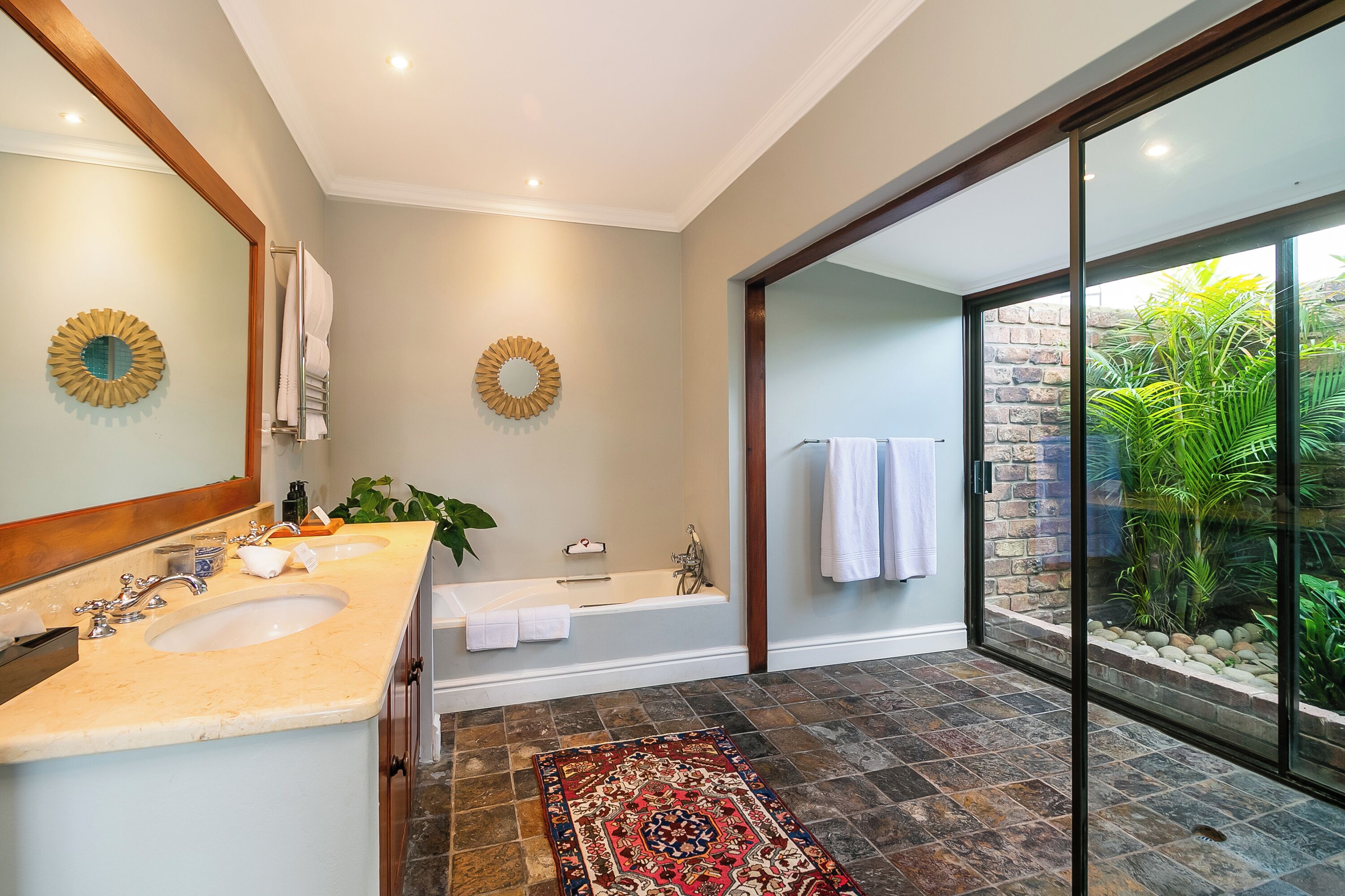 Un baño con dos lavamanos, una bañera y un gran ventanal de vidrio que da a un jardín.