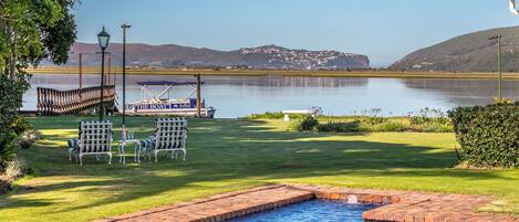 Una piscina con vista a un muelle y un área verde con sillas.