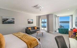 Habitación de hotel moderna con cama, sofá, una pequeña mesa de centro y balcón con vistas al mar.