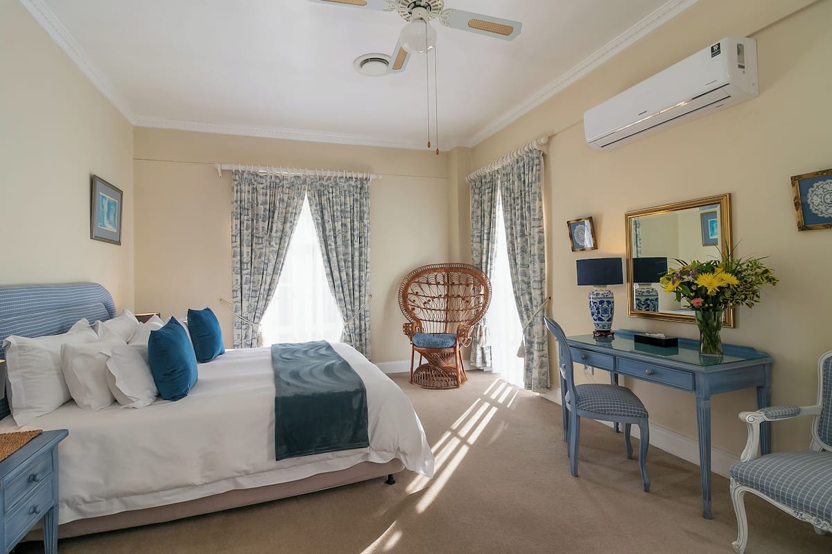 A bedroom with a bed, a desk, a chair, a ceiling fan, and an air conditioning unit.