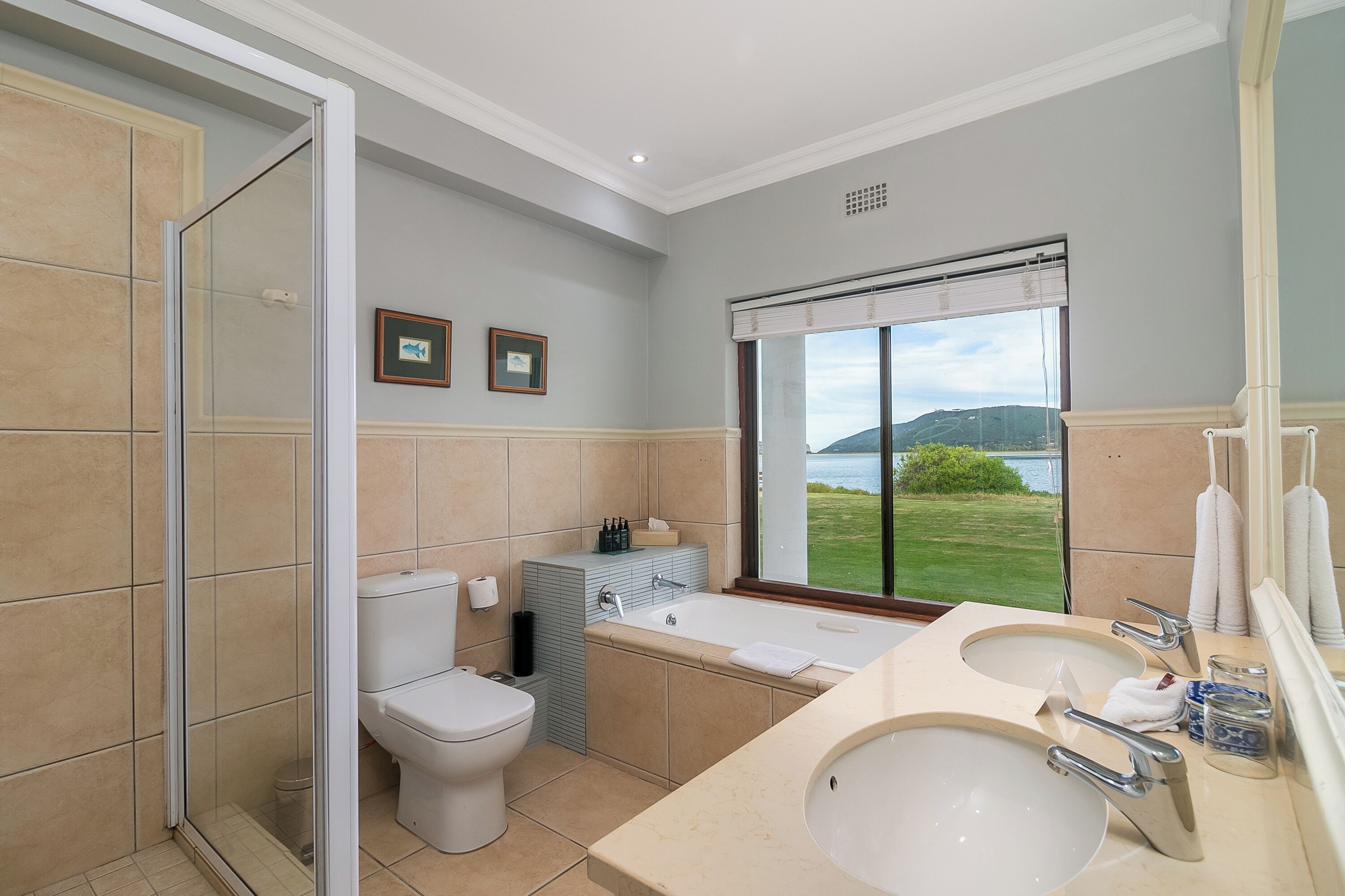 Un baño con una bañera grande, dos lavamanos, un inodoro y una ducha. Hay una ventana con vistas al exterior.