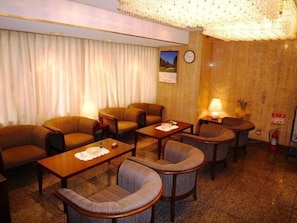 Habitación de hotel con zona de estar que incluye cuatro sillones y dos mesitas, suelo de madera y un ventanal con cortinas.