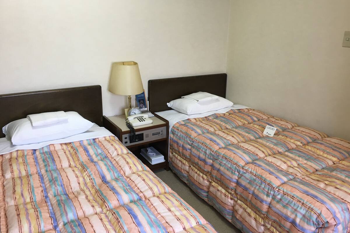 Une chambre d’hôtel avec deux lits, chacun doté de draps à rayures, une table de chevet avec une lampe, un téléphone et un livre.