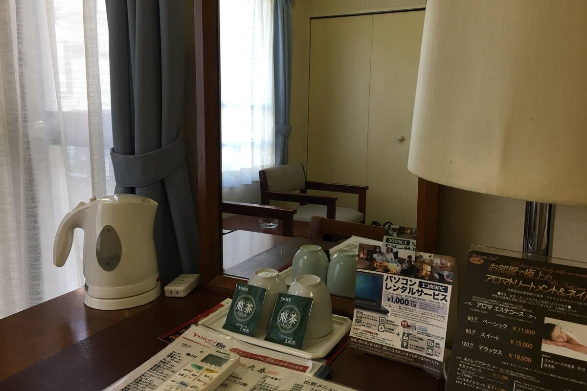 Une chambre d’hôtel avec une table en bois, une bouilloire blanche, une lampe et un menu.