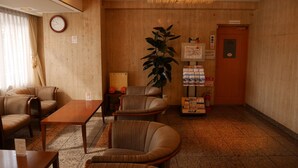 Een hotel lobby met zitplaatsen, een klok, een plant, een brandblusser en een deur met daarop de tekst 