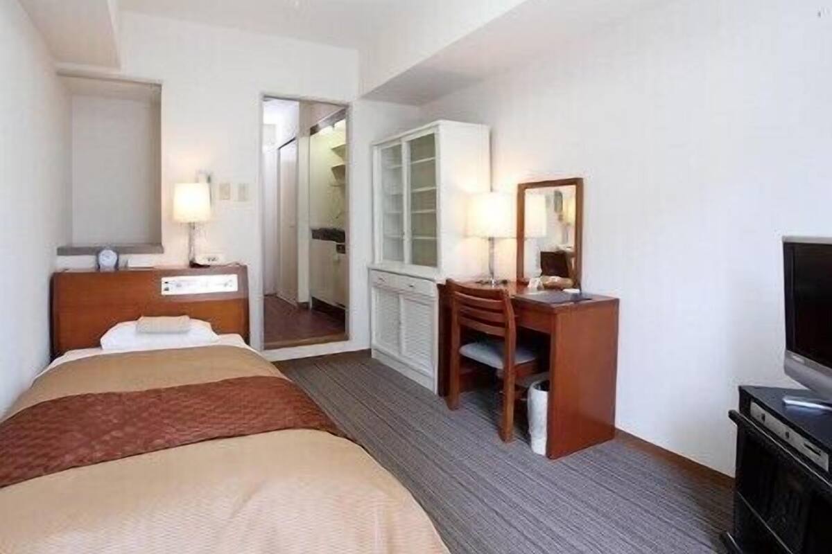 Une chambre d’hôtel comprenant un lit, un bureau avec une chaise, une télévision et une armoire.
