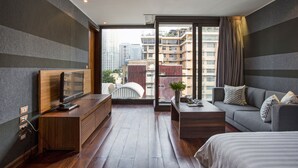 A modern hotel room with a wooden desk, a sofa, a bed, and a large window offering a city view. - LUXX Langsuan Hotel (Bangkok)