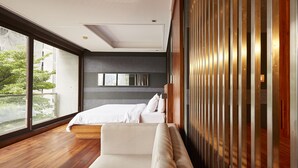 A modern bedroom with a large bed, a sofa, and a view of the outdoors through large windows. - LUXX Langsuan Hotel (Bangkok)