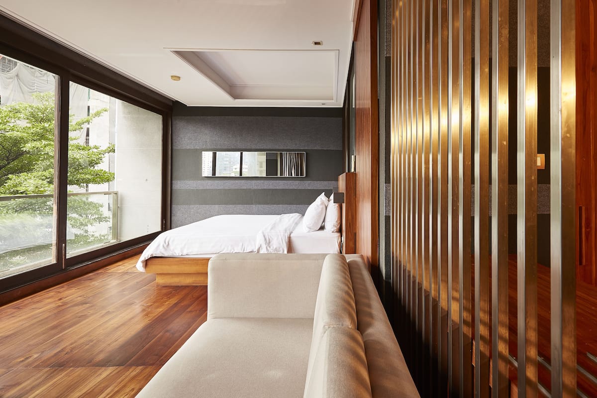 Un dormitorio moderno con una cama grande, un sofá y vistas al exterior a través de amplios ventanales.