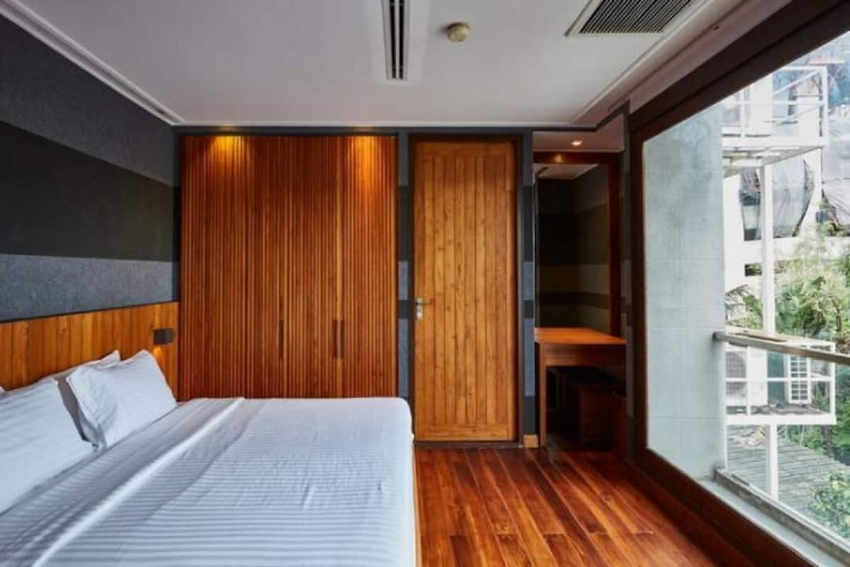 Una habitación de hotel moderna con una cama grande, paneles de madera y un balcón con vistas a la ciudad.