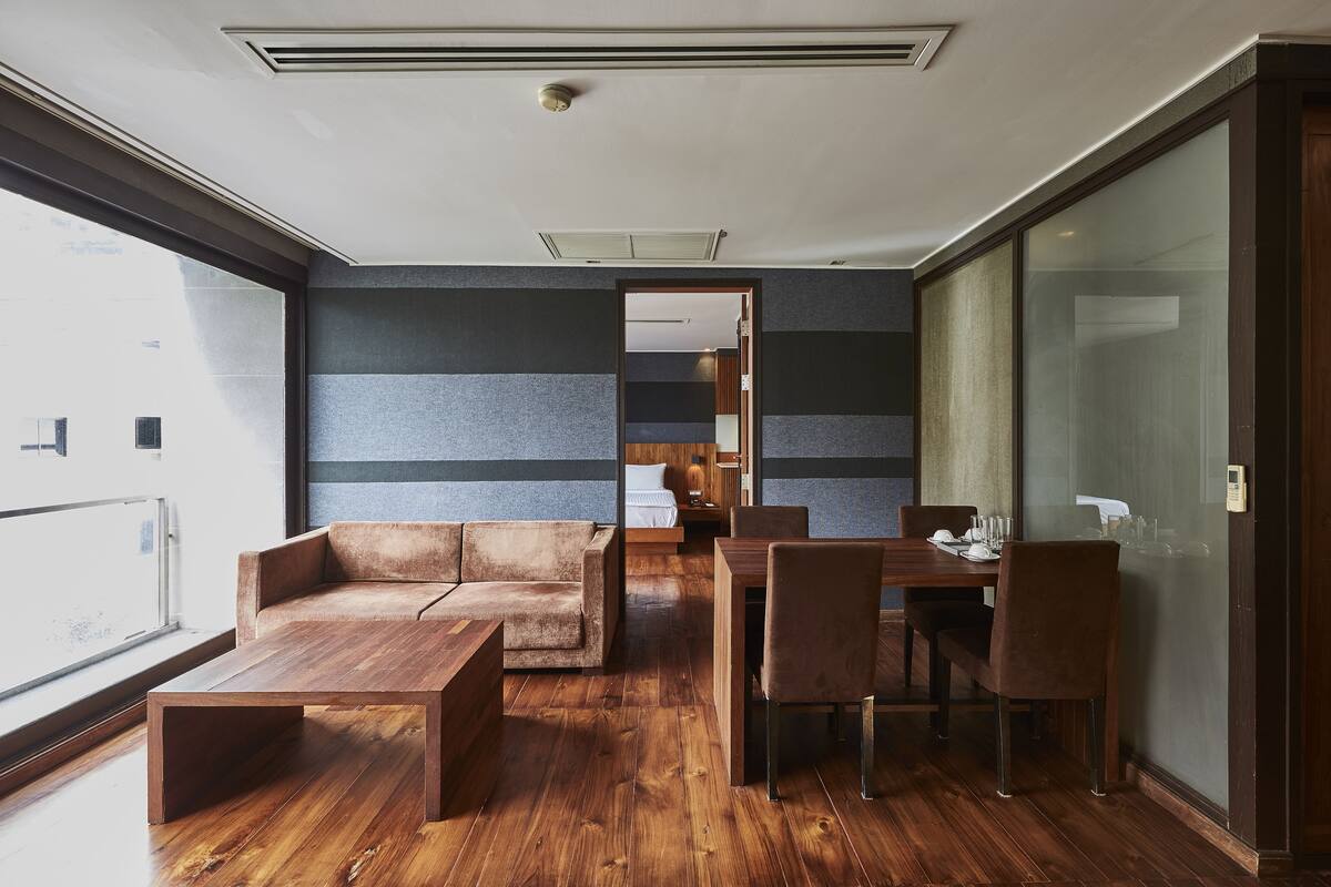 Un interior moderno con suelo de madera, un sofá, una mesa de comedor con sillas y un separador de vidrio.