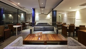 A modern restaurant with a mix of seating options including tables and couches, a laptop on a table, and a decorative wall with vertical elements. - LUXX Langsuan Hotel (Bangkok)