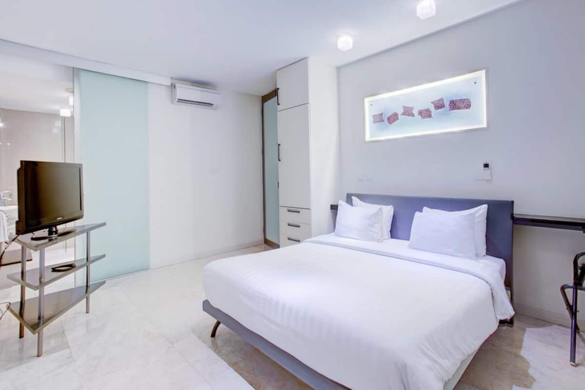 A modern hotel room with a large bed, a TV on a stand, a desk, and a wall-mounted artwork.