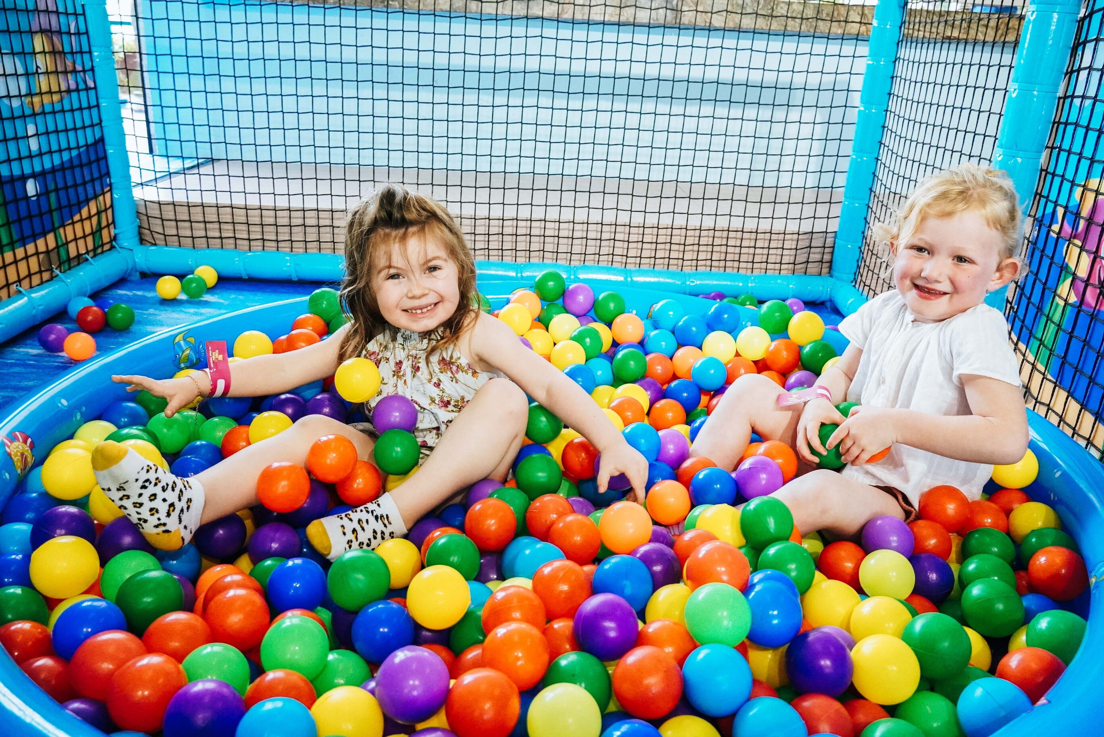 Dos niños jugando en una piscina de pelotas llena de bolas multicolores.