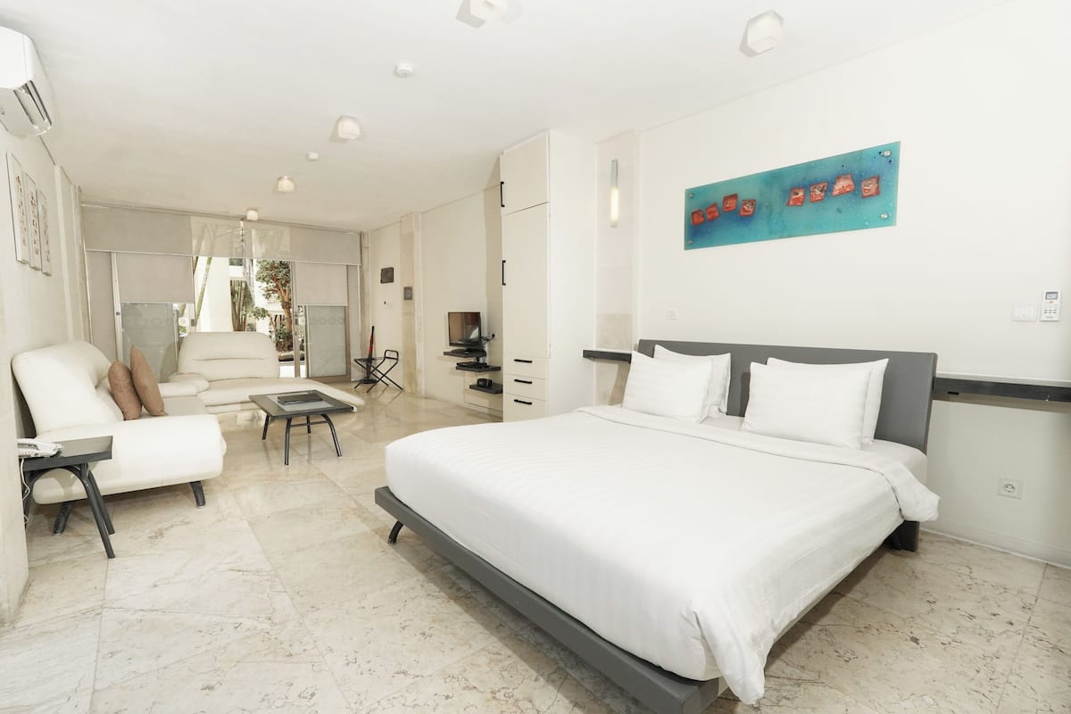 A modern hotel room with a large bed, a sofa, a desk, and a dining area.