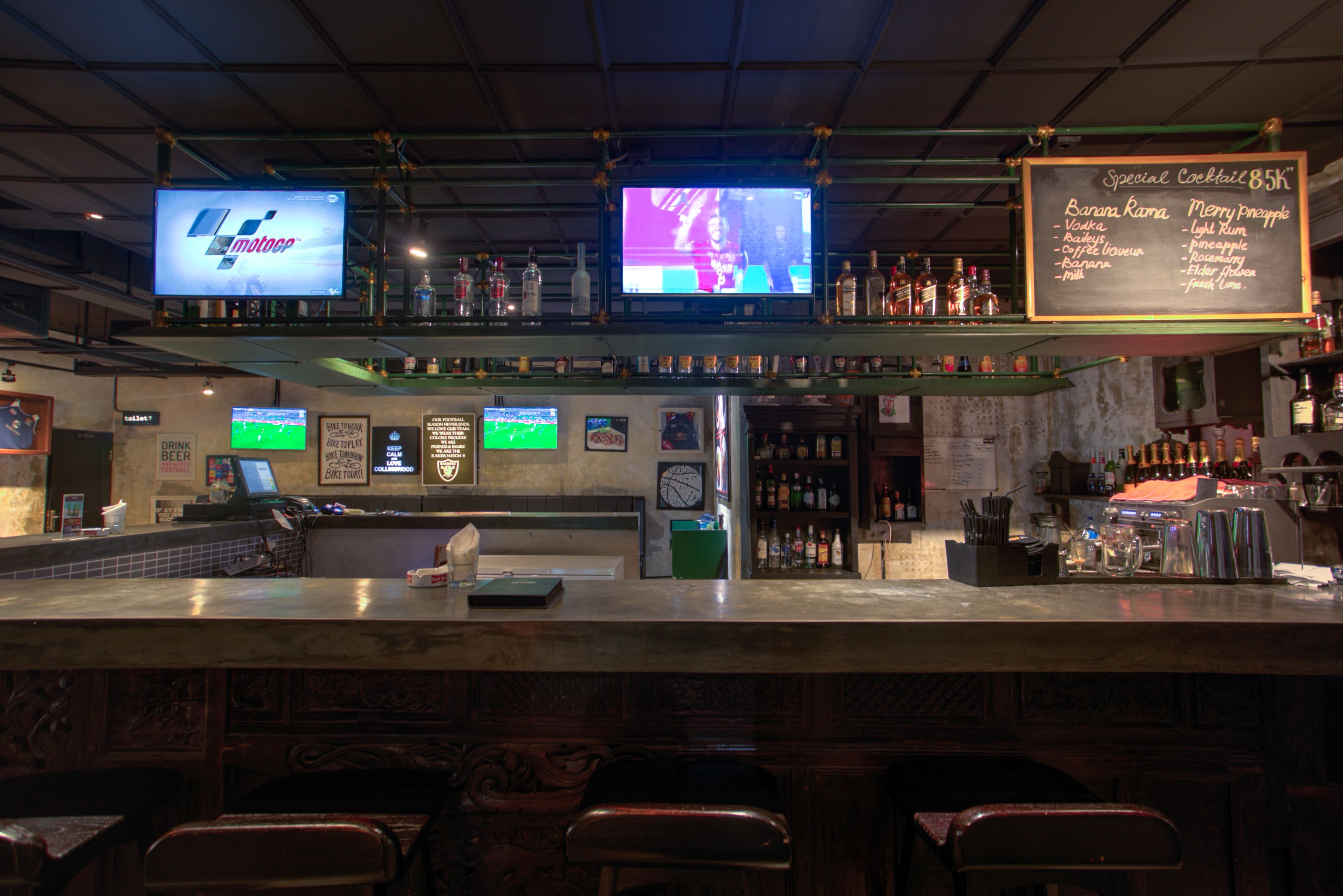 A bar area with two TVs, a chalkboard menu, and bar stools.