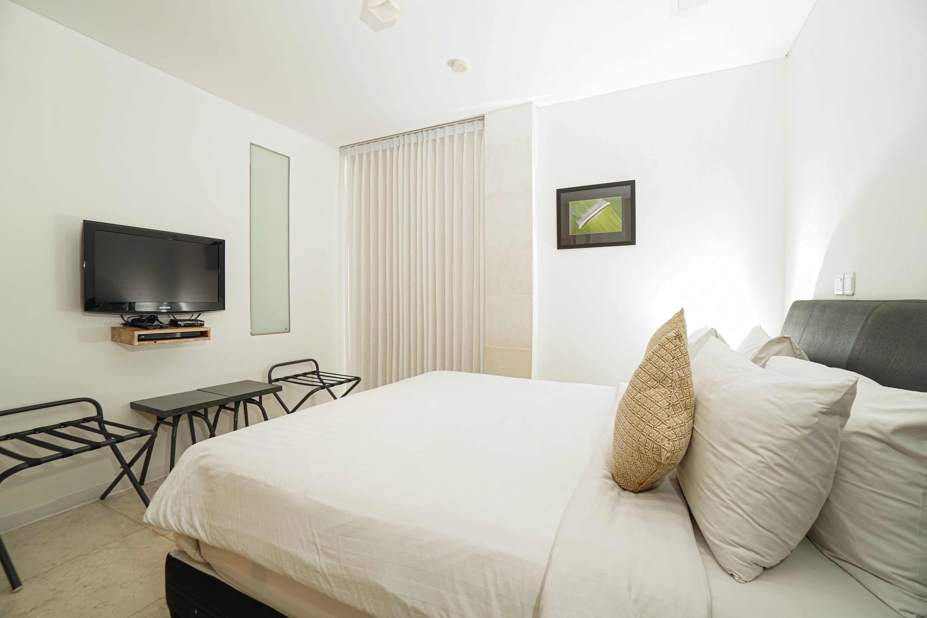 Une chambre d’hôtel moderne équipée d’un lit, d’un bureau, d’une chaise, d’une télévision et d’une fenêtre avec des stores.