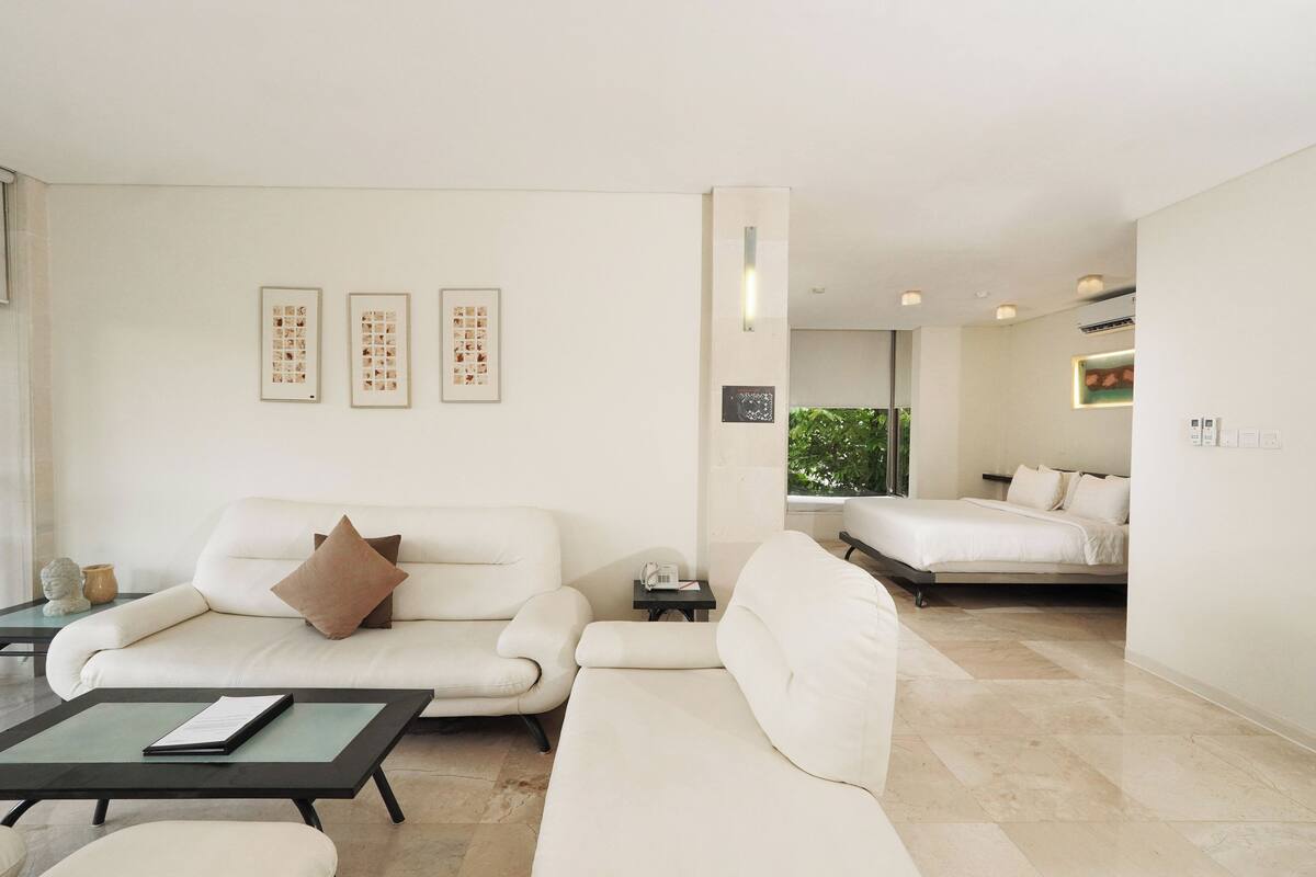 A modern hotel room with a sofa, a bed, a small table, and a wall-mounted phone.