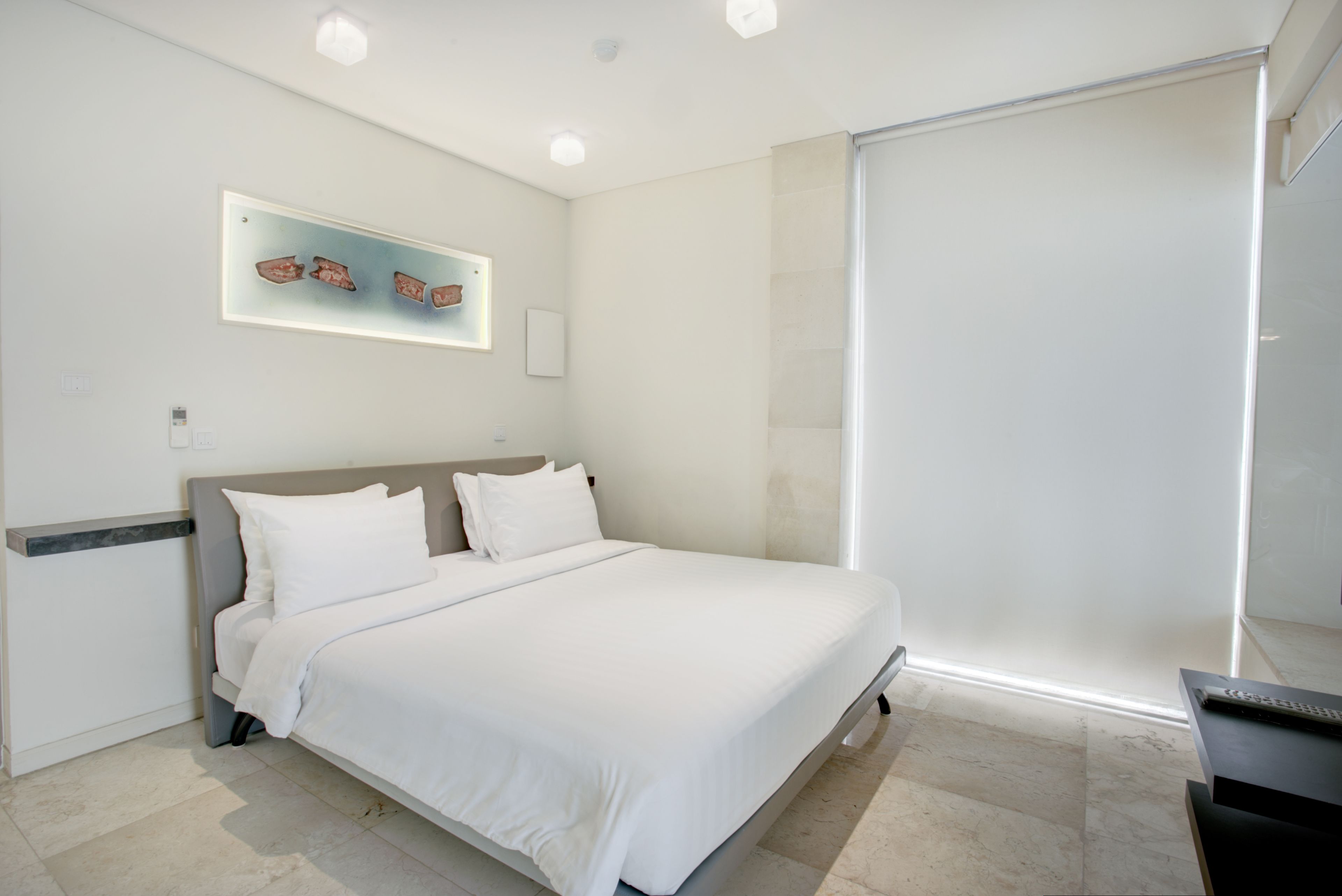 A modern bedroom with a large bed, a bedside table, a wall-mounted light fixture, and a sliding door.