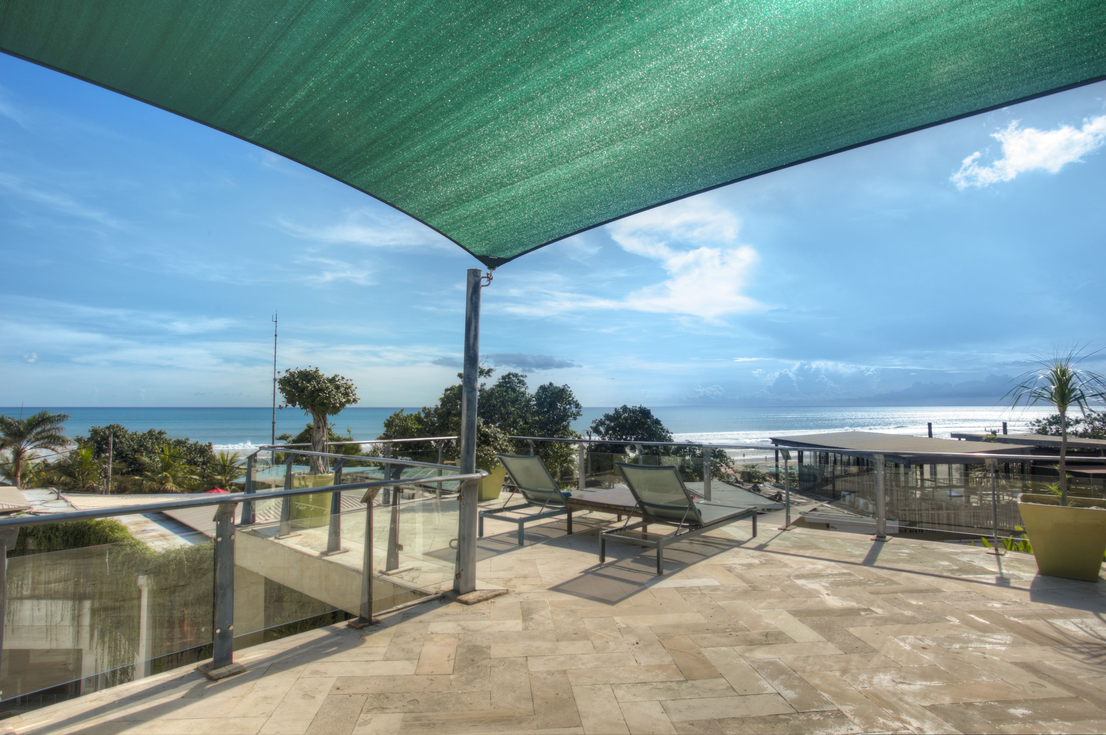 A terrace with a view of the ocean, outdoor seating, and a shaded area.
