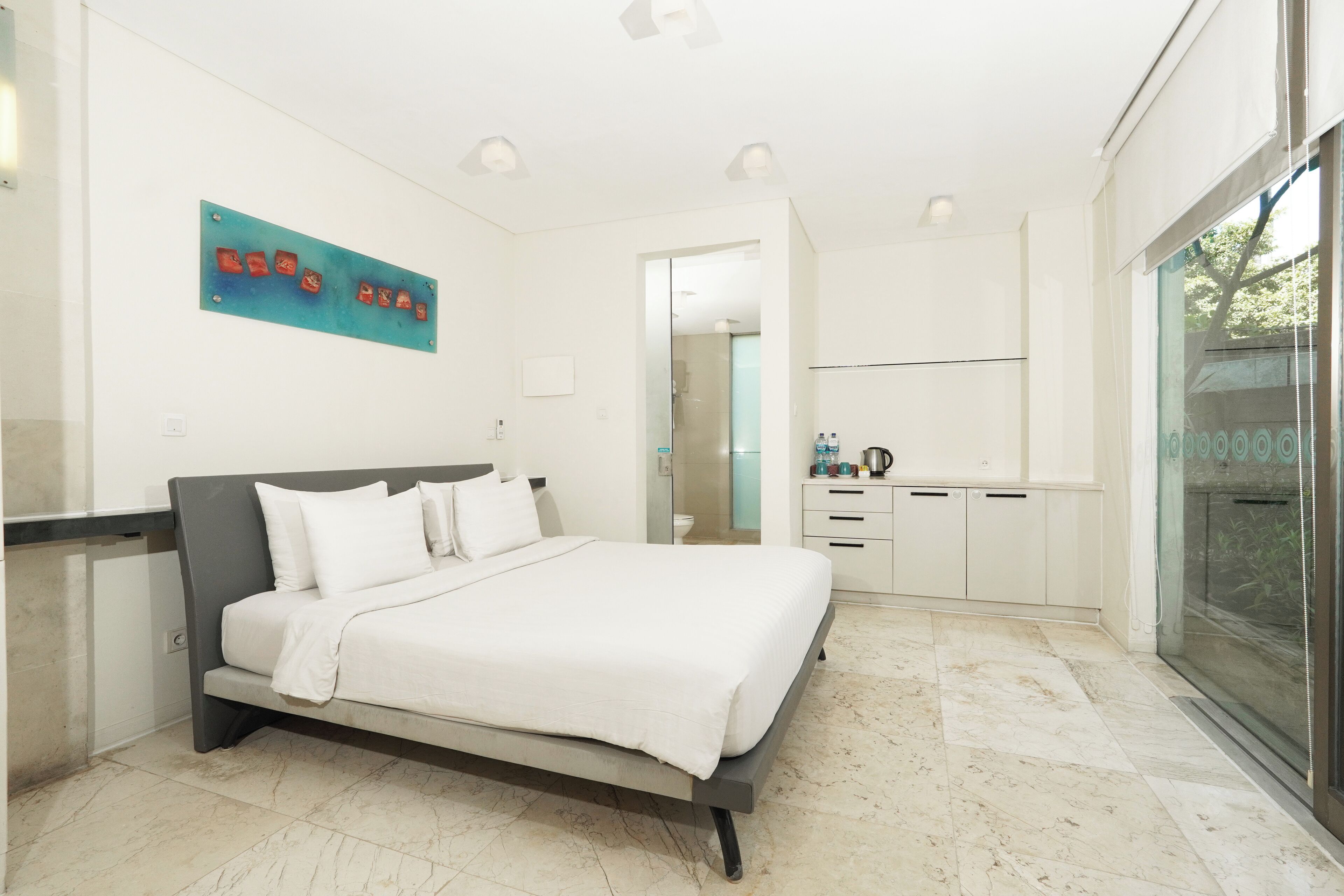 A modern bedroom with a bed, a small kitchenette, and a bathroom visible through an open door.