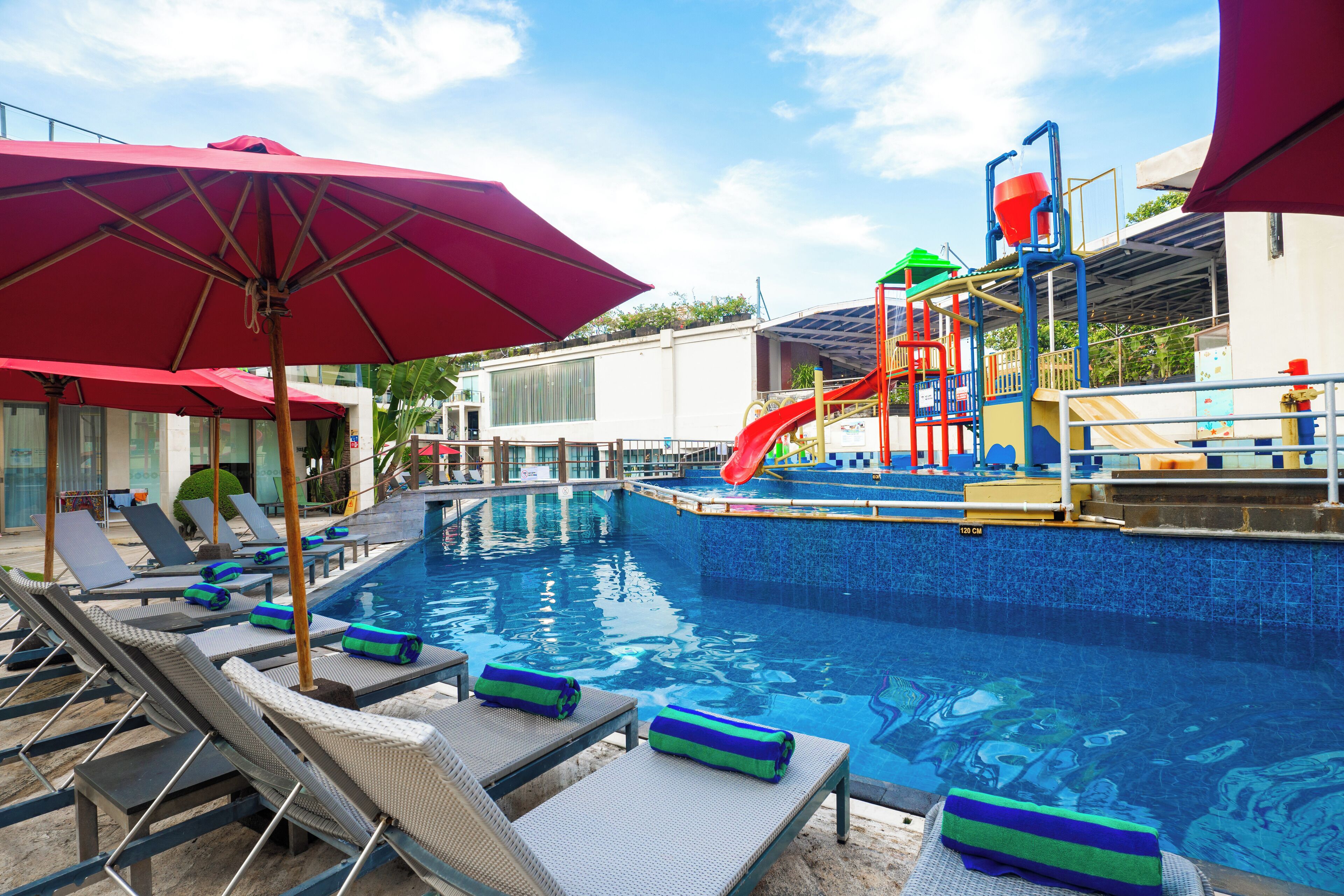 A swimming pool with lounge chairs and umbrellas, a slide, and a play structure.
