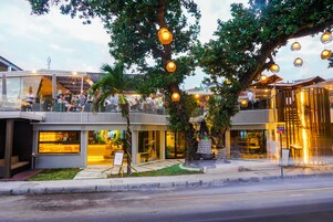Un edificio moderno con fachada de vidrio, asientos al aire libre y luces esféricas colgantes.