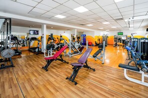 Une salle de sport équipée de divers appareils d’exercice, notamment des tapis de course, des appareils de musculation et des bancs.
