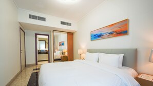 Et hotelværelse med en stor seng, et natbord, en lampe, et billede på væggen og et badeværelse, der kan ses gennem en åben dør.