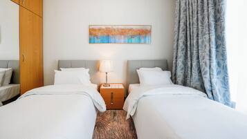 A hotel room with two beds, a nightstand with a lamp, a wooden wardrobe, and a painting on the wall.
