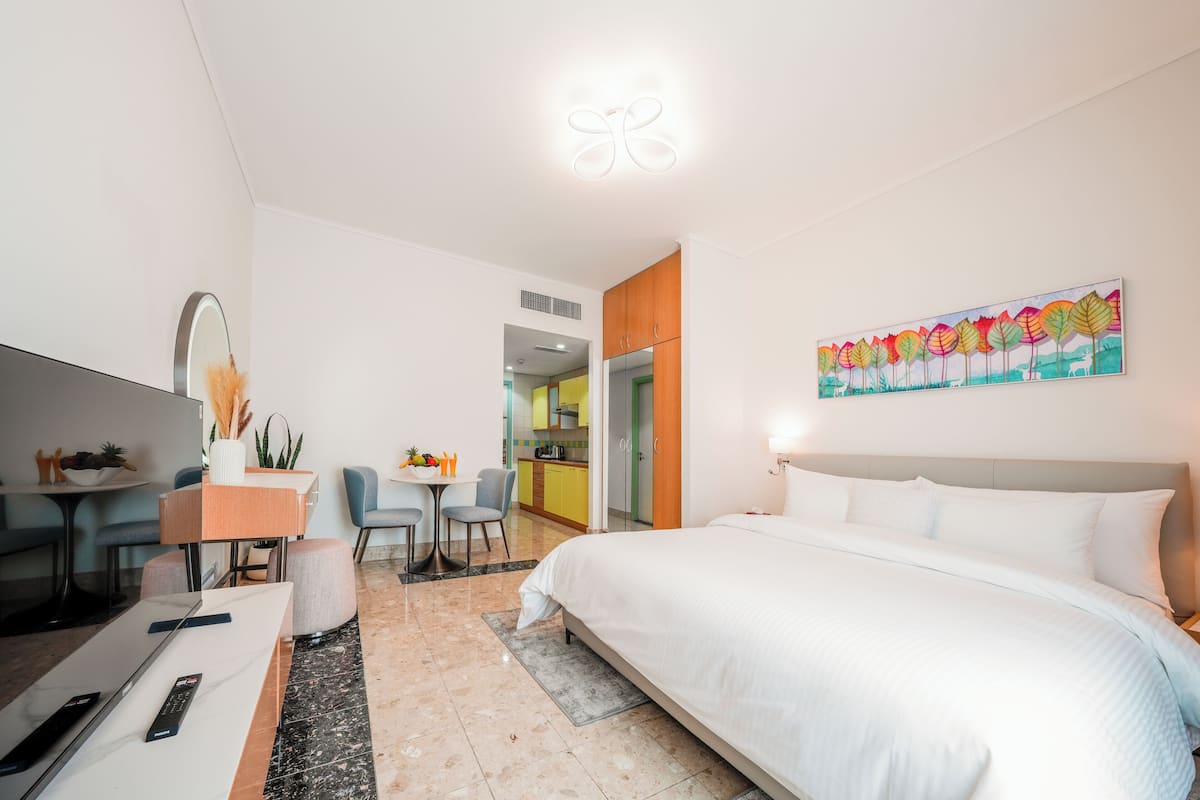 Une chambre d’hôtel moderne avec un grand lit, un bureau avec un ordinateur, un coin repas et une cuisine à l’arrière-plan.