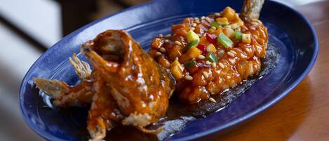 A blue plate with two fried fish and a sauce with diced vegetables on a wooden table.