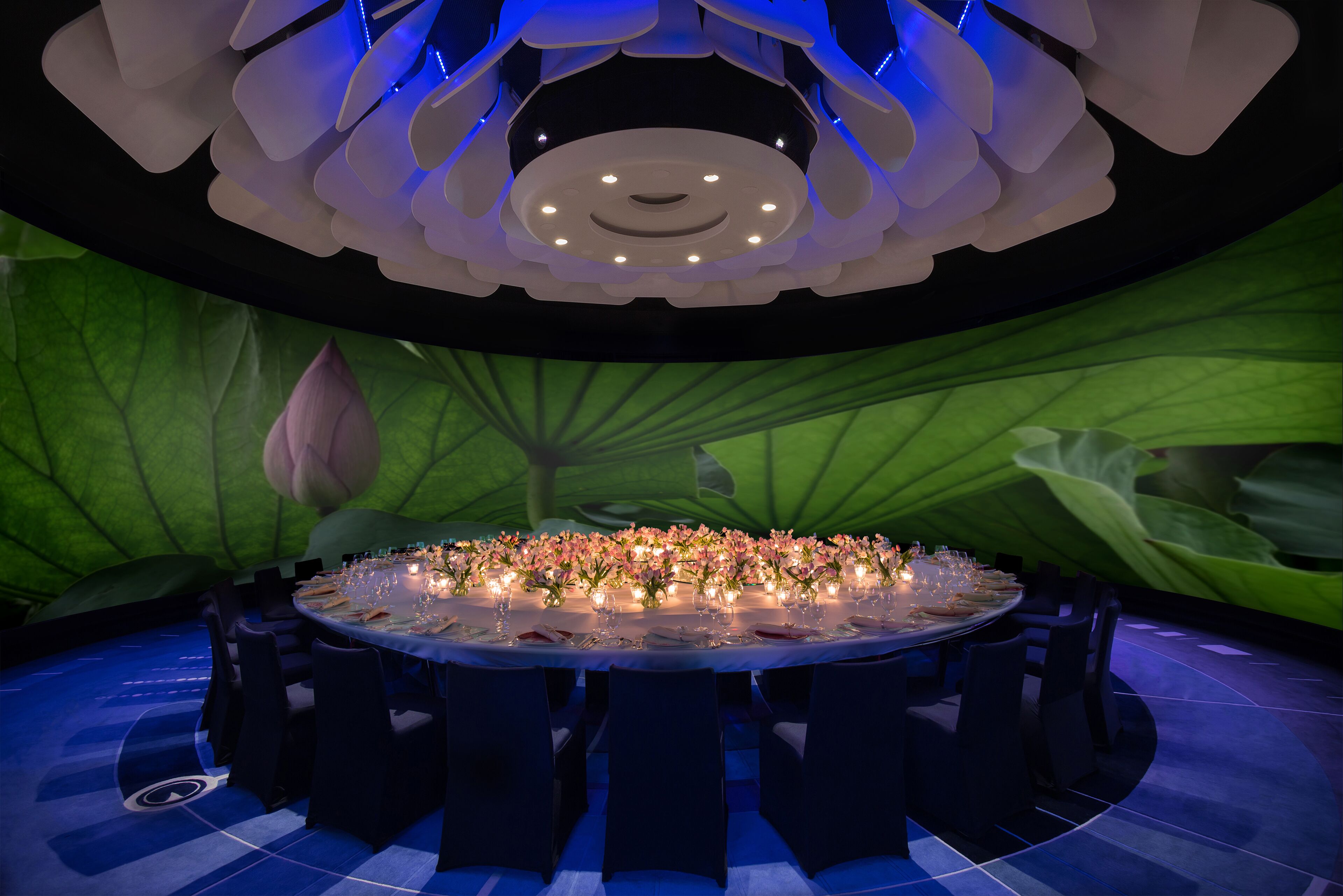A round table set for a formal event, surrounded by dark chairs, with a floral arrangement and candles on the table.