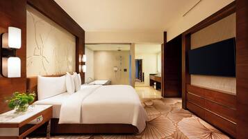 A hotel room with a large bed, a desk with a lamp, a TV, and a bathroom visible through an open door.