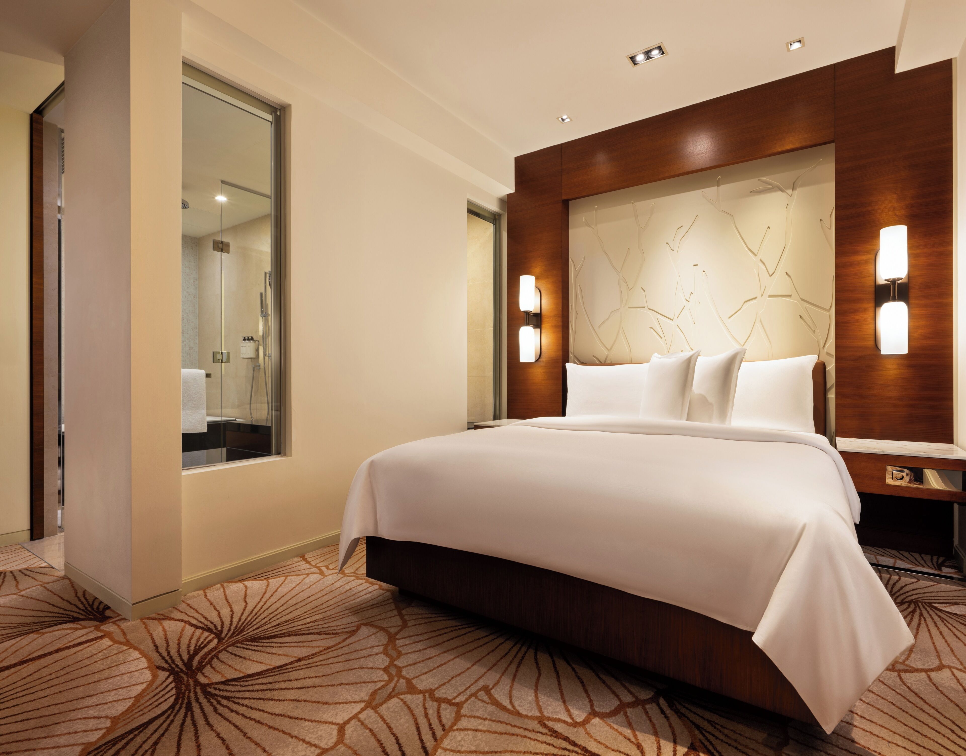 A hotel room with a large bed, a wooden headboard, a mirror, and a wall-mounted light fixture.