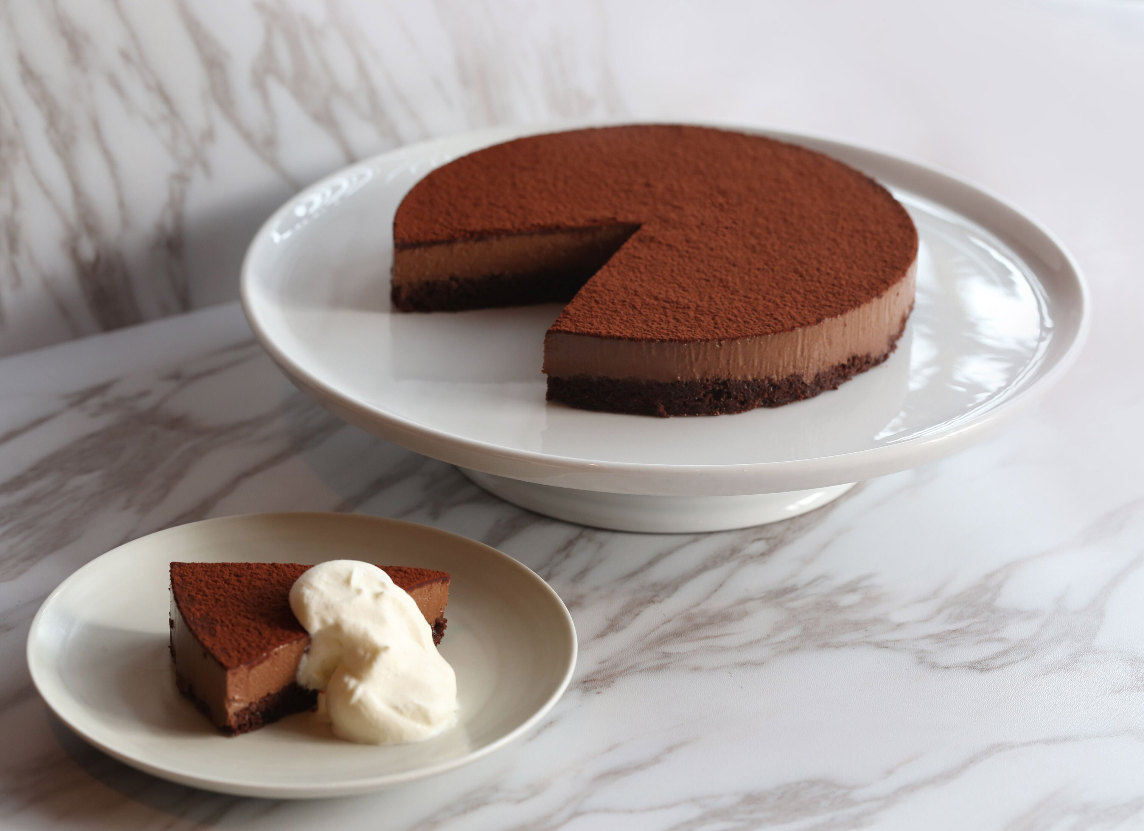 Une part de gâteau au chocolat avec une garniture crémeuse, présentée sur une assiette, posée sur une surface en marbre.