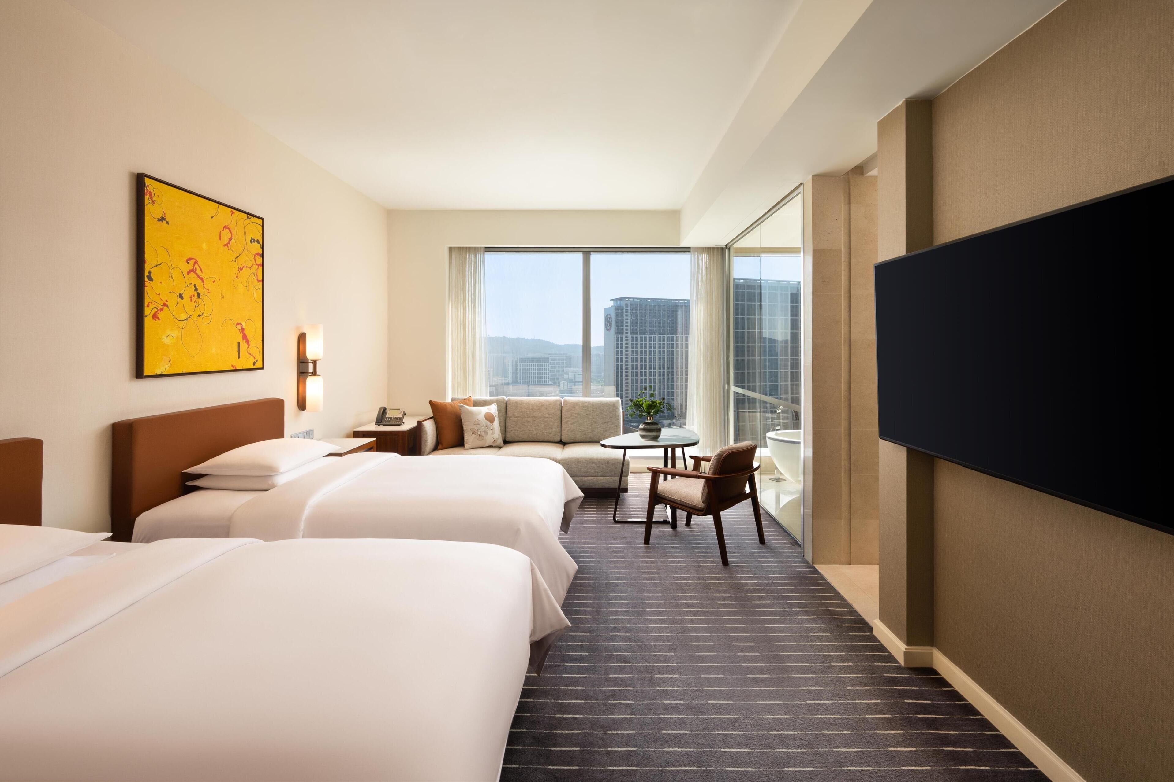 A hotel room with two beds, a sofa, a small table, and a TV.
