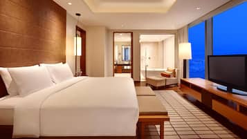 Habitación de hotel con una cama grande, televisión, zona de estar y vistas a la ciudad.