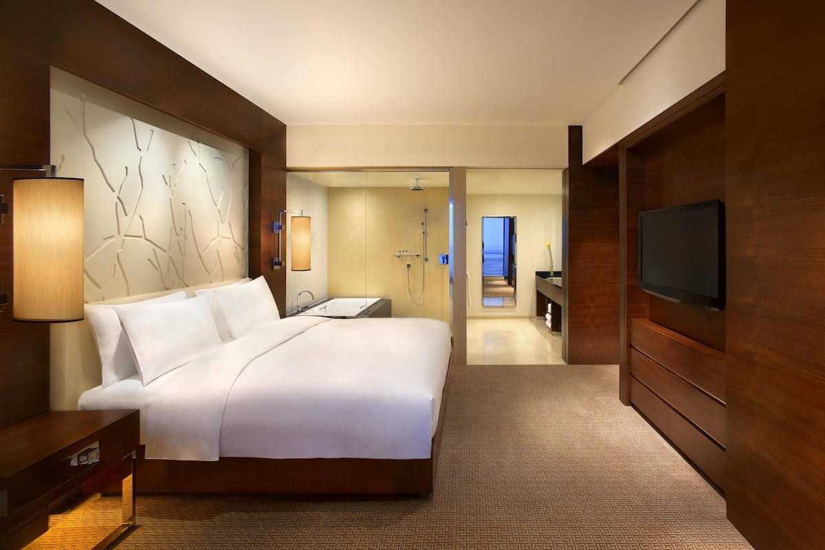Una habitación de hotel moderna con una cama grande, televisión, baño con ducha y vista al mar.