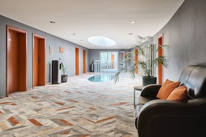 A hotel lobby with a central pool, a seating area with a leather sofa, and a reception desk.